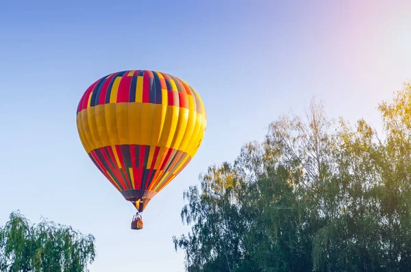 Πολύχρωμο αερόστατο πετά στο μπλε του ουρανού πάνω από τα δέντρα — Φωτογραφία Αρχείου