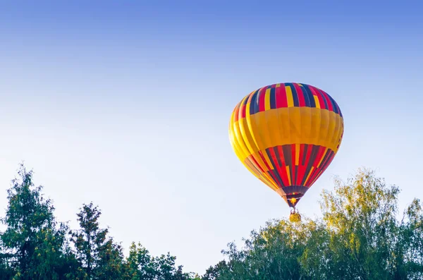 Renkli sıcak hava balonu ağaçların yukarıda mavi gökyüzünde uçuyor — Stok fotoğraf