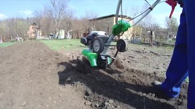 Adam bahçedeki toprağı bir dümenciyle işliyor, toprağı ekime hazırlıyor.