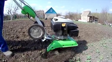 Adam bahçedeki toprağı bir dümenciyle işliyor, toprağı ekime hazırlıyor.
