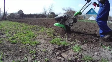 Adam bahçedeki toprağı bir dümenciyle işliyor, toprağı ekime hazırlıyor.