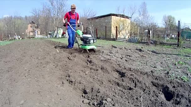 人間は耕運機で庭の地面を耕し 播種のための土壌を準備する — ストック動画