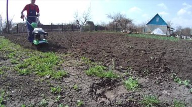 Adam bahçedeki toprağı bir dümenciyle işliyor, toprağı ekime hazırlıyor.