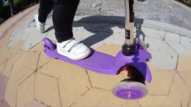 Kaldırımda scooter süren küçük bir çocuğun bacakları.