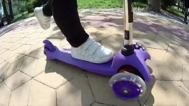 Kaldırımda scooter süren küçük bir çocuğun bacakları.