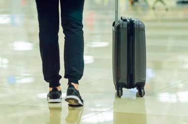 Bir kız havaalanı salonunda yürür ve tekerlekler üzerinde bir bavul taşır. Tatil seyahati