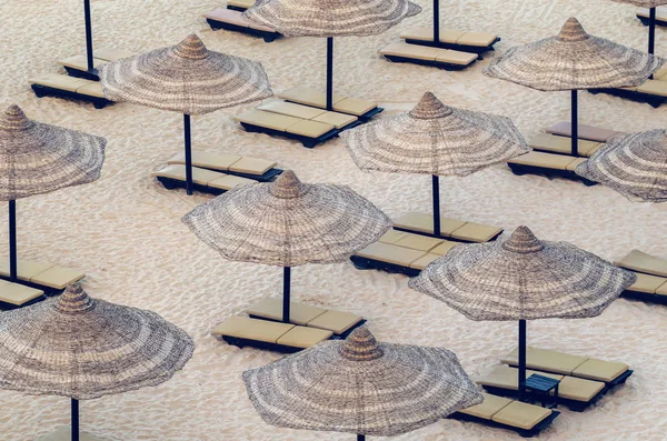 Reed umbrellas with loungers on a beautiful sandy beach — Stock Photo, Image