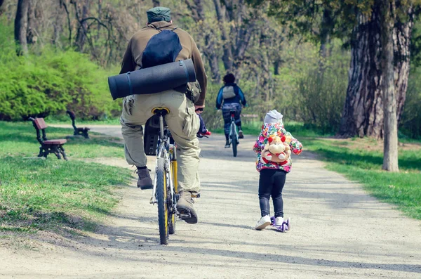 A man on a bicycle and a little girl on a scooter ride in the spring park. — Stock Photo, Image