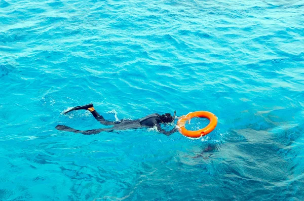 Un joven en traje de buceo y aletas nada en el mar sosteniendo la boya salvavidas —  Fotos de Stock