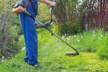 Bahçıvan bahar bahçesinde bir budama makinesiyle çimleri biçer.