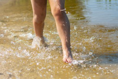 Bir çocuk nehir kıyısında koşar ayaklarıyla su sıçratır.