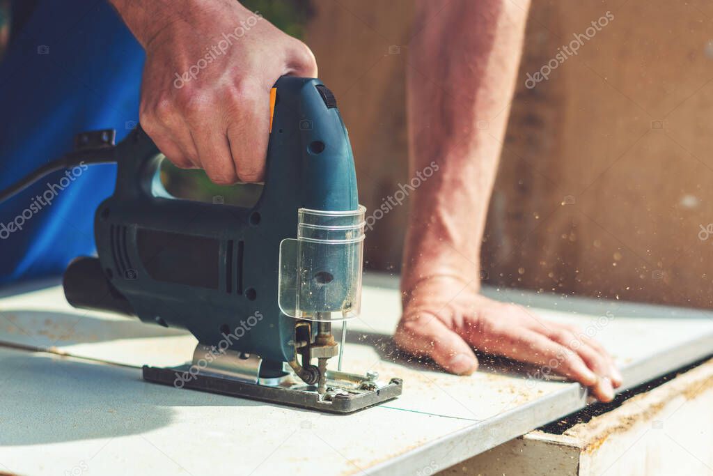 A carpenter saws a wooden cloth with an electric jig saw.