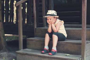 Şapkalı küçük kız oturur ve eski ahşap bir evin verandasında hayal kurar..