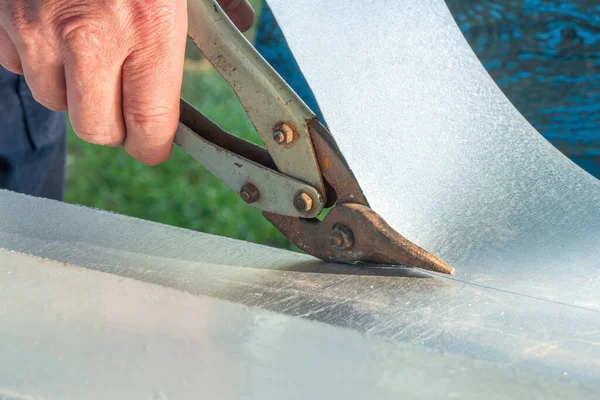 Bir işçi metal makasla teneke bir yaprak kesiyor..