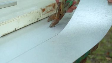 Bir işçi metal makasla teneke bir yaprak kesiyor.