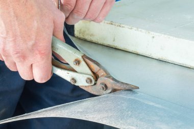 Bir işçi metal makasla teneke bir yaprak kesiyor..