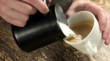 Kahve bardağındaki baristanın elleri ahşap masada.
