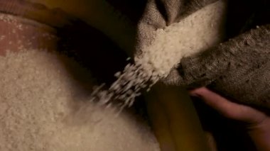 Ağır ağır inleyen pirinç çuvalı yığının üstüne düşüyor.