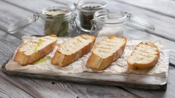 Жидкость льется на хлеб ломтики багета на бумажном оливковом масле для брускетты — стоковое видео