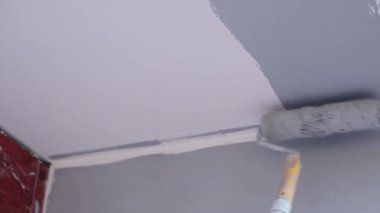 İnşaatçı beyaz duvarı gri renge boyuyor.