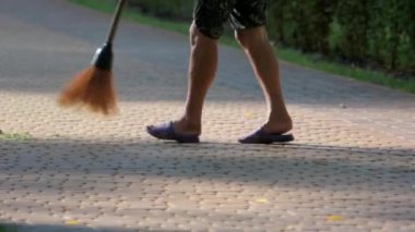 Parkın caddesindeki kaldırımlardaki çimenleri süpürüyor.