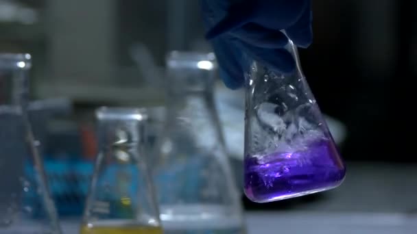 Рука тримає колбу з рідким склянкою з фіолетовою рідиною — стокове відео