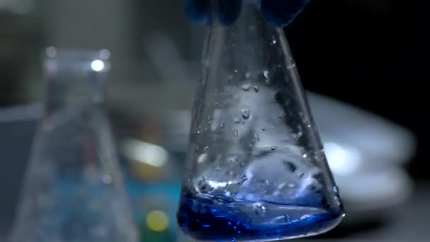 Líquido em uma mão de copo em luva segurando flask trabalho em um laboratório — Vídeo de Stock