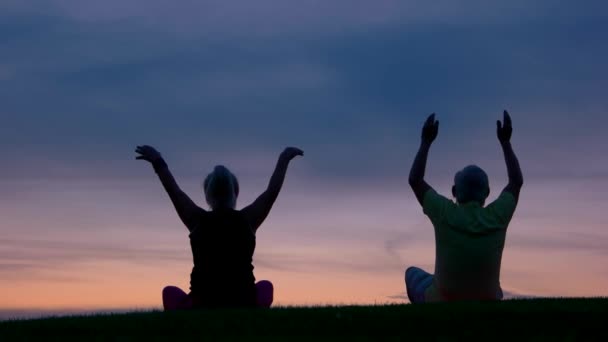 Para robi jogi ludzie siedzi na tle zachodu słońca — Wideo stockowe