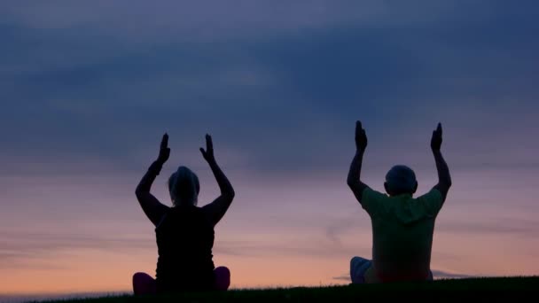 Para robi jogi ludzie siedzi na tle zachodu słońca — Wideo stockowe