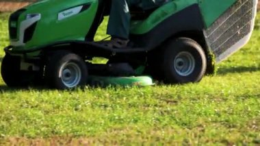 Çim biçme makinesine binip yeşil çim biçme makinesini kapatıp çimleri biçiyorum.
