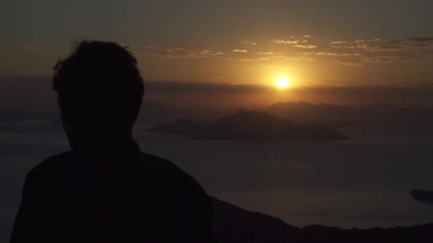 Ένας άντρας στην κορυφή ενός λόφου να βλέπει τη θέα του ηλιοβασιλέματος στον ορίζοντα — Αρχείο Βίντεο