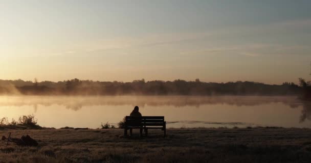 Persona sentada sola en un banco frente a un lago — Vídeos de Stock