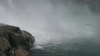 Nehirdeki kayaların üzerine çağlayarak su dökülüyor.