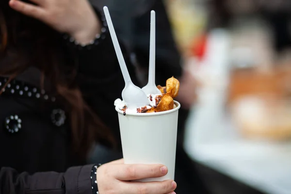 Bir kadının eli plastik kaşıkla kağıt bardakta waffle ve dondurma tutuyor.