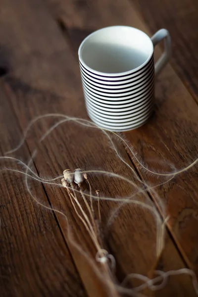 Kuru gelincik çiçekleri ve boş kupa ahşap bir masada.