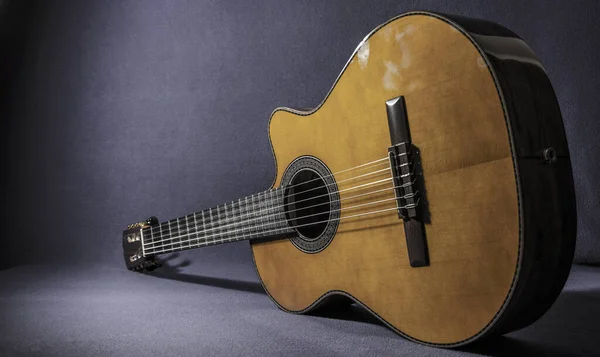 Beautiful electro-acoustic guitar resting on the floor, resting on its side and diagonally. Photograph taken from the front on a dark background, lighting only the guitar