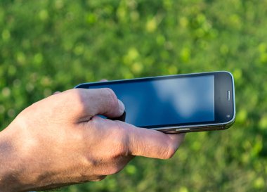 Beyaz adamın elinde cep telefonu var. Arka planı bulanık. Siyah ekran üzerinde çimen tıkırtısı var.