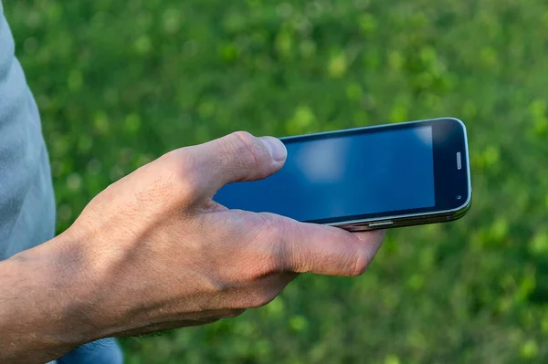 Bulanık çimen arka planlı, elinde cep telefonu olan beyaz bir adam.
