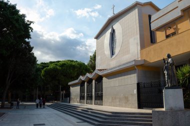 Modern Hıristiyan kilisesi. Dışarıda yaşlı insanlar ve meydanda bir heykel var.