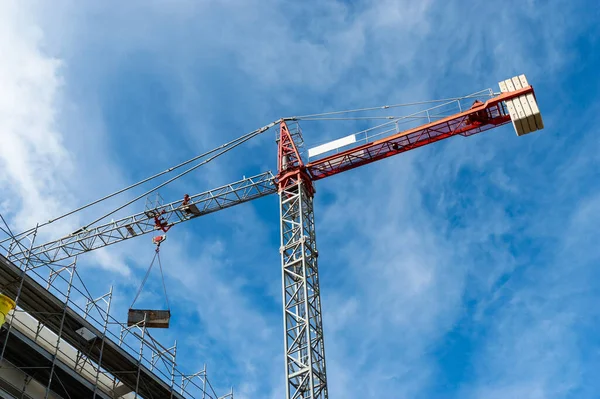 Red tower crane building against a blue sky with clouds. Building crane apartment