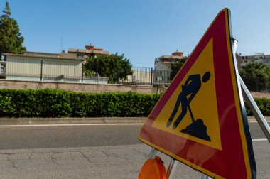 Üçgen işaretini kapat. Çalışmalar devam ediyor. Yol çalışması, yol işaretleri. İş yerindeki erkekler. Kentsel caddede çalışma için bazı tabelalar.