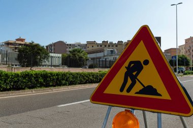 Üçgen işareti çalışıyor. Yol çalışması, yol işaretleri. İş yerindeki erkekler. Kentsel caddede çalışma için bazı tabelalar.