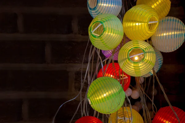 Colorful paper lantern fairy lights close up plugged into wall. Switched on colourful light & dark.