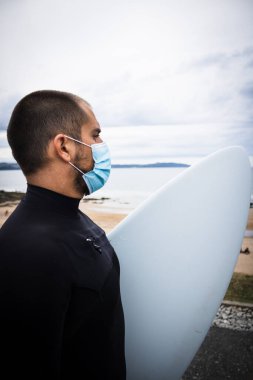 Sörf tahtası sörfçüsü, maskeli adam ve sahilde dalgıç kıyafeti.