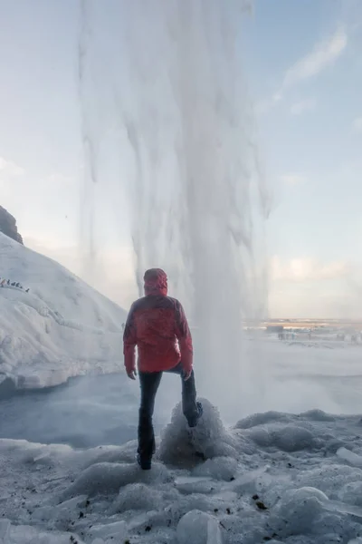 Maschio turista in abiti caldi in piedi dietro enorme maestosa cascata Seljalandfoss in Islanda — Foto Stock