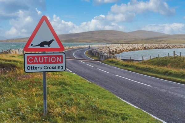 Caution Otters Crossing red triangle road sign by causeway, North Uist Outer Hebrides Western Isles Scotland UK — стоковое фото