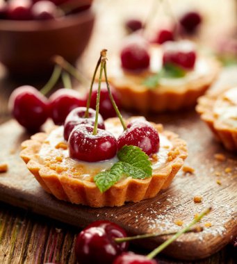 Taze kirazlı tartlar, vanilyalı krema ve karamel, ahşap bir masada lezzetli bir tatlı, yakın plan.