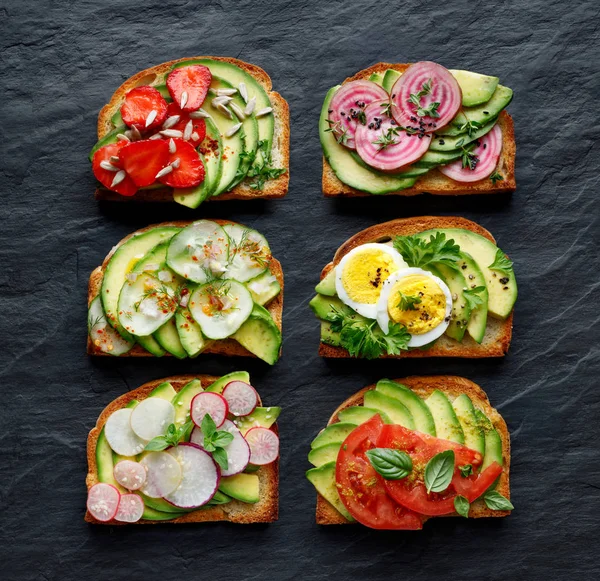 Avocado Sandwiches Toasts Various Vegetarian Toppings Black Stone Background Top — Stock Photo, Image