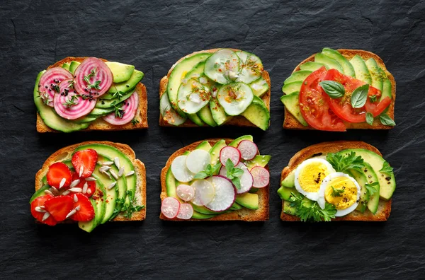 Бутерброди Авокадо Тости Різними Вегетаріанськими Начинками Фоні Чорного Каменю Вид — стокове фото