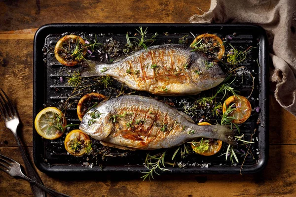 Grilled  fish, sea bream, dorada with the addition of spices, herbs and lemon on the grill plate located on a wooden background,  top view. Healthy eating concept